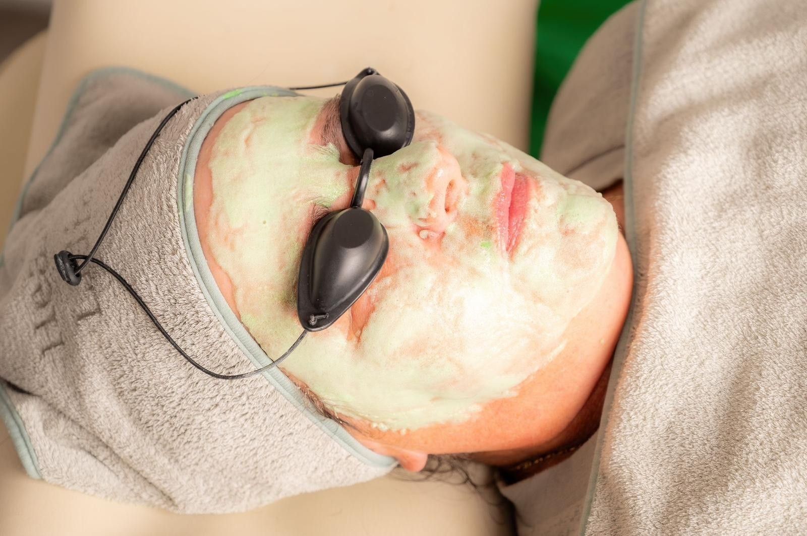 Kundin mit Gesichtsmaske und Schutzbrille w&auml;hrend einer Behandlung